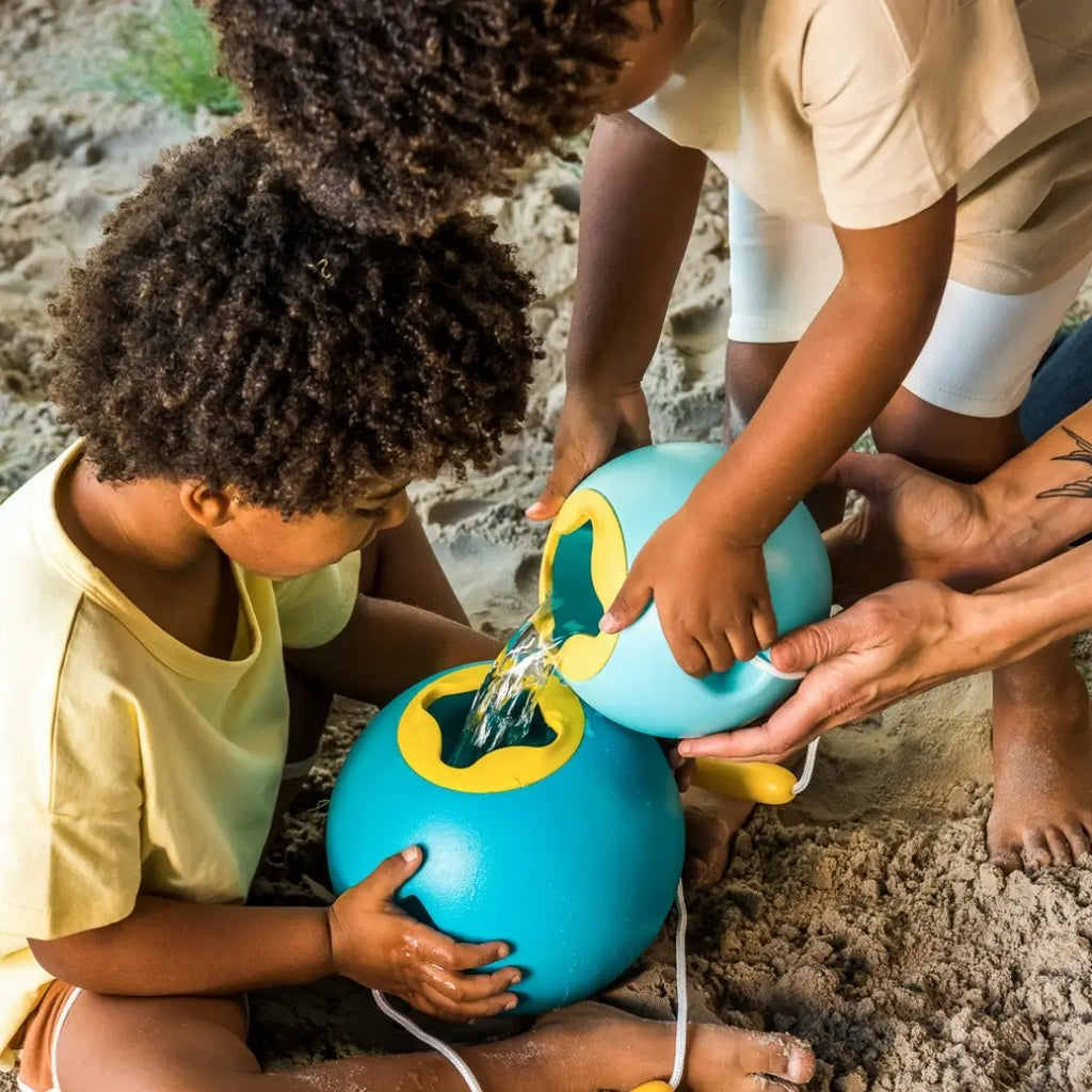 Child pouring water from banana blue Mini Ballo bucket during outdoor play