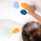 Child sticking foam fish to tub wall during bath play