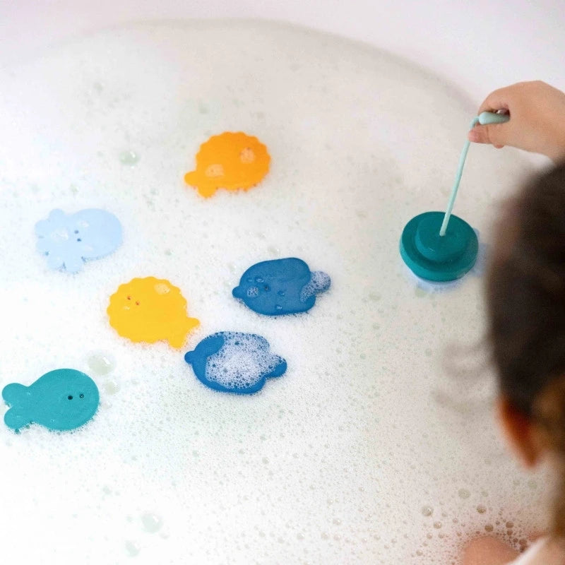 Toddler catching floating foam fish with soft fishing rod in bathtub