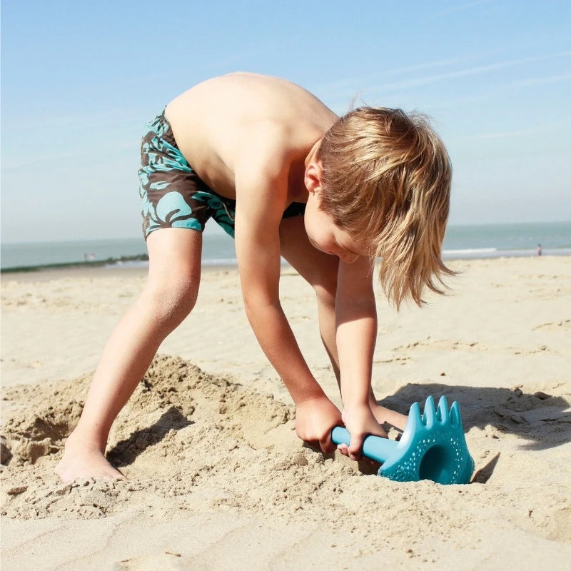 Toddler scooping sand with Triplet tool during beach play