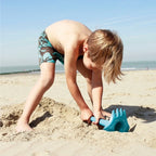 Toddler scooping sand with Triplet tool during beach play