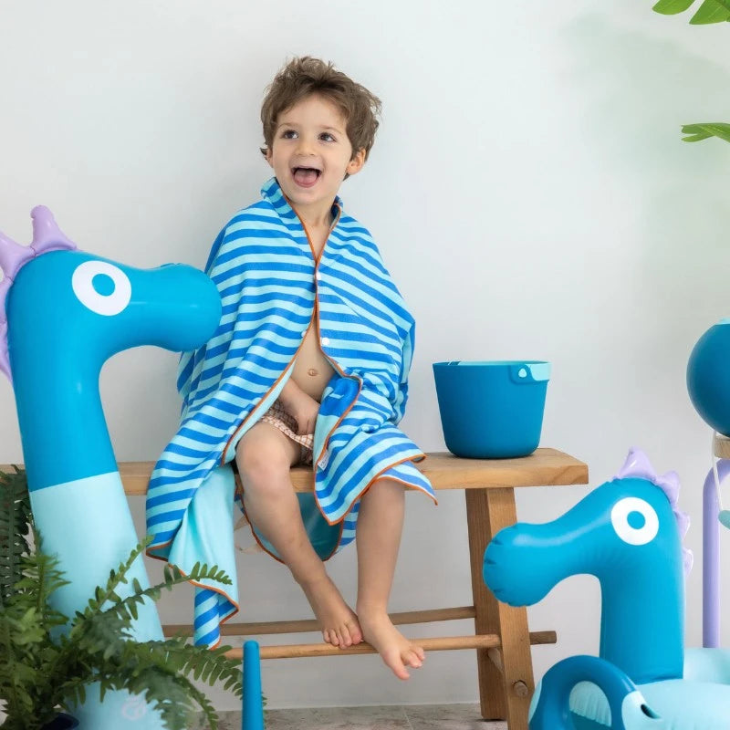 Child wrapped in a blue striped towel sitting on a chair with blue dragon-shaped chairs and a bowl in the background.