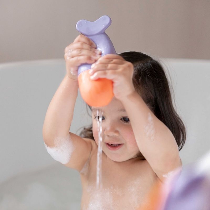 Toddler squeezing a soft silicone whale bath toy during bath time