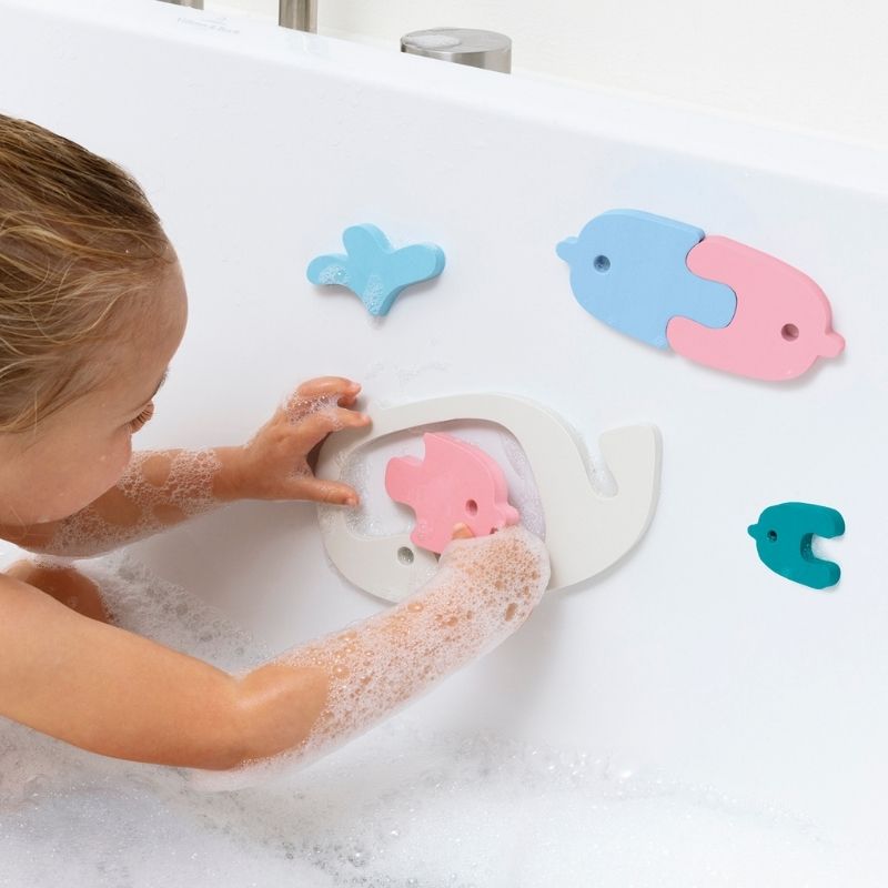 Toddler sticking floating whale puzzle pieces to the bath wall