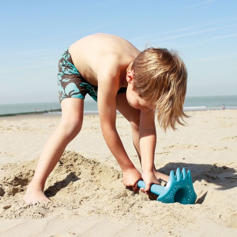 Child playing on a beach with blue sand digging toys