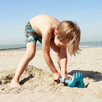 Child playing on a beach with blue sand digging toys