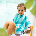 Toddler sitting on a beach towel with poncho keeping sand away